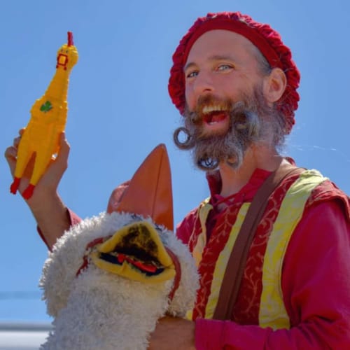 A man with curly beard and mustache holding a rubber chicken